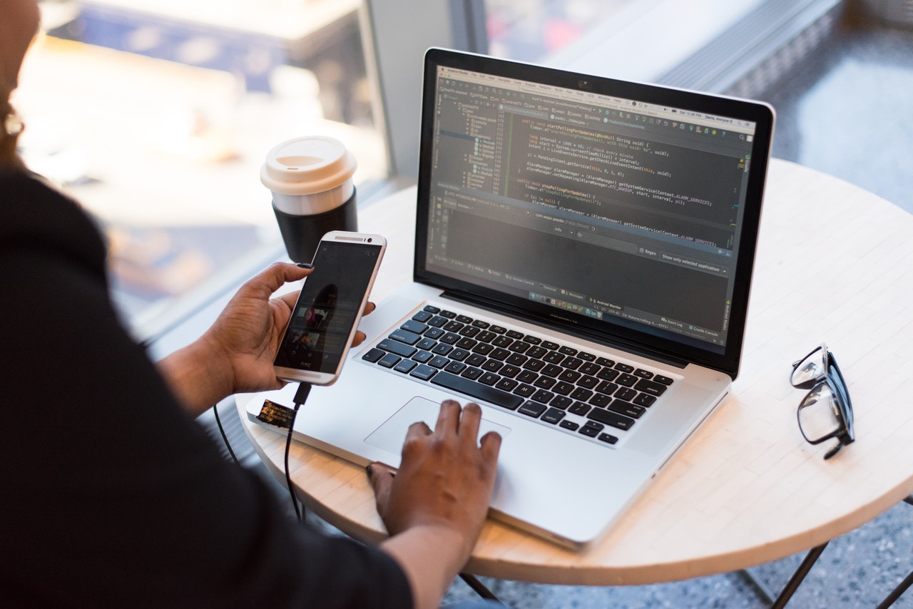 Developer checking her mobile while on a Macbook in a coffee shop.